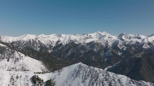 Wide aerial panorama of snow-covered Sayan Mountains and forested ridges near Peak Galina, Arshan village, Republic of Buryatia, Russia on a clear winter day