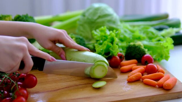 Cutting fresh zucchini slices on wooden board with colorful farm vegetables around