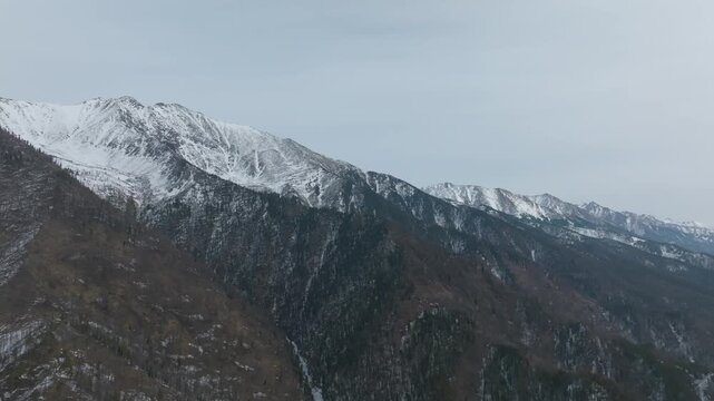 Aerial view of the snow-covered mountain ridge and forested slopes at Peak of Love near Arshan village, Republic of Buryatia, Russia, under an overcast sky