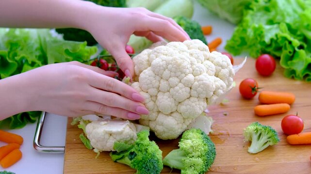 Breaking cauliflower head into pieces on rustic table with fresh garden ingredients