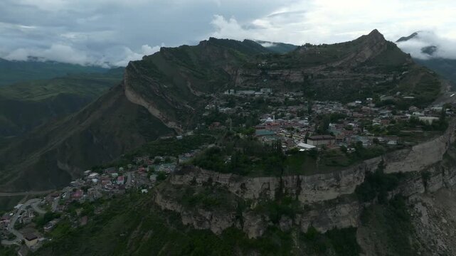 Drone footage of Gunib aul on a dramatic cliff plateau surrounded by green Caucasus Mountains and low clouds, Republic of Dagestan, Russia, scenic travel landscape