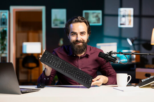 Smiling content creator filming keyboard review in personal studio, ready to start testing it. Cheerful technology guru showcasing computer peripheral to audience on niche online channel