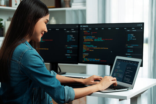 Smiling young Asian in IT developer creating with typing online information on laptop with coding program data of application, wearing jeans shirt. surrounded by safety analysis two screen. Stratagem.