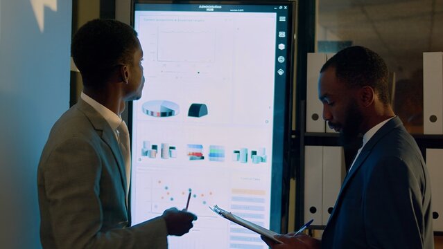 Teamworking businessmen working on company revenue statistical graphics in modern office during nightshift. Colleagues solving important project tasks, checking charts on digital screen
