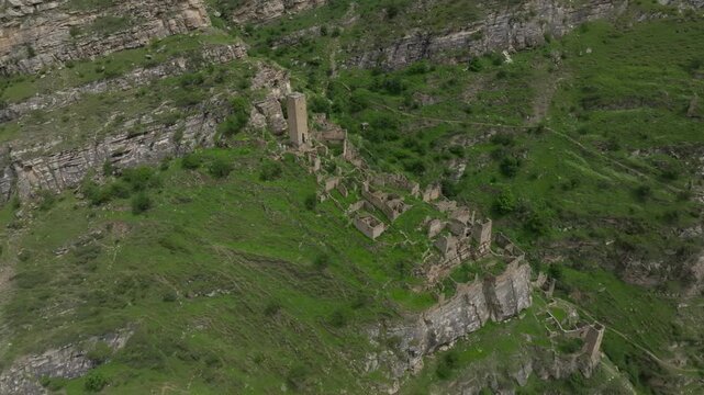 Drone footage of the abandoned stone aul of Kahib on a steep green mountainside, with ancient towers and ruined houses in Dagestan, Russia, Caucasus region