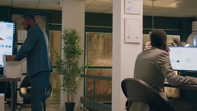 Upset worker holding box filled with desk belongings bidding farewell to colleague during last nightshift in office after being laid off. Sad businessman getting consoled after being fired from job