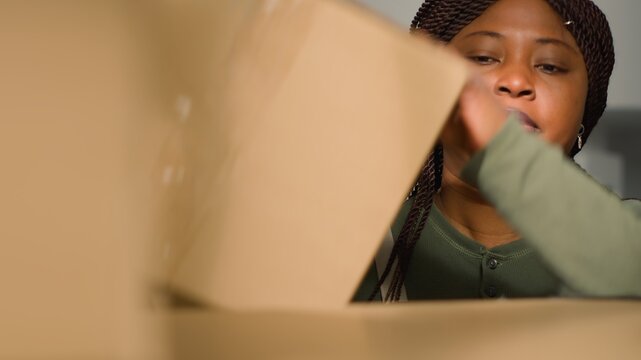 Close up shot of warehouse picker arranging cardboard boxes full of merchandise ready to be shipped to clients. Hardworking employee in repository using ladder to put parcels on cabinet shelves
