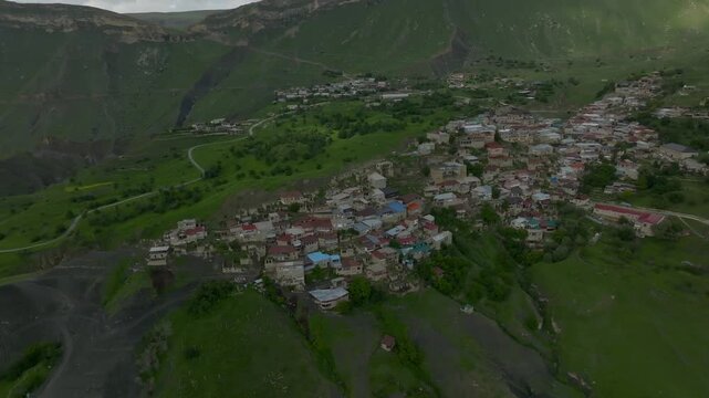 Drone footage of Chokh rural settlement nestled on mountain slopes with clustered houses and winding roads, surrounded by lush green hills in Dagestan, Russia