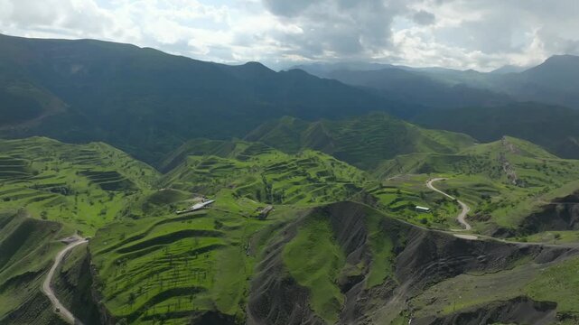 Drone footage of Chokh village with traditional houses on a steep mountain slope, green valleys and dramatic ridges under cloudy sky in Dagestan, Russia, Caucasus