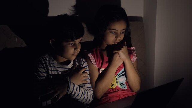 Cute brother and sister are frightened while viewing something unbelievable - Screen Time. Indian siblings feeling scared while watching a horror movie on their laptop in the darkness - kids lifest...