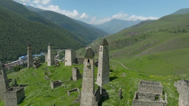 Drone footage of the medieval Erzi tower complex with stone watchtowers and ruins on green mountain slopes in Ingushetia, Russia