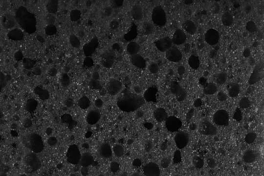 Macro, closeup of black foam sponge texture with porous, spongy and bubbly surface pattern suitable for abstract background design. Foamed polyurethane material surface