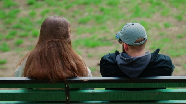 A close perspective from behind shows a couple sitting side by side on a park bench, quietly sharing a moment together
