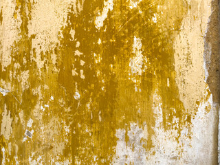 A rustic wall surface features layers of distressed mustard yellow paint peeling away to reveal weathered white and grey plaster underneath with textures © anammarques