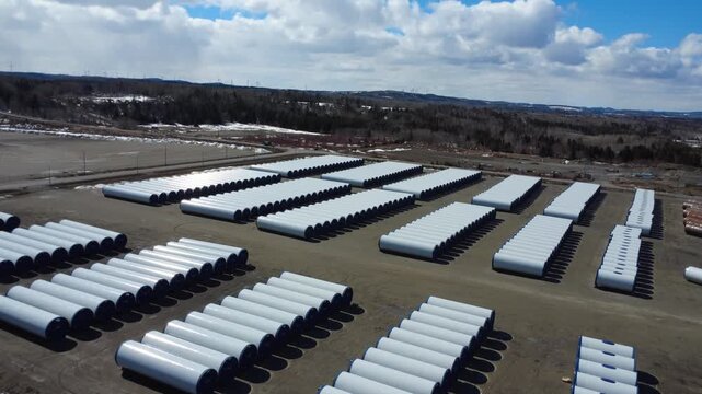 Aerial drone footage showing rows of white wind turbine masts in a large industrial storage area, highlighting renewable energy logistics and infrastructure in Quebec, Canada.