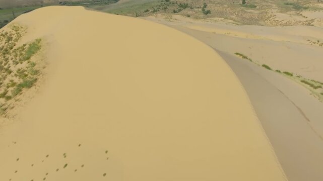 Drone footage of the Sarykum sand dune with wind-shaped ridges and footprints, surrounded by sparse vegetation near Makhachkala, Republic of Dagestan, Russia