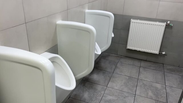 Row of White Ceramic Urinals in Clean Public Restroom &mdash; Slow Motion Push In | Modern Men Bathroom with Gray Tile Wall and Heating Radiator