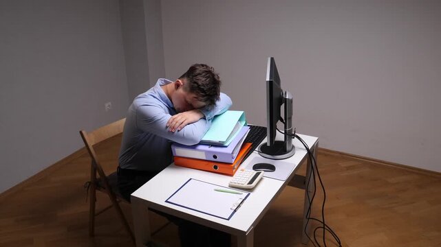 Stressed employee feeling burnout and exhaustion, resting head on a stack of business folders at a simple office workstation late at night, needing sleep from fatigue