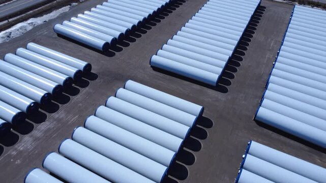 High-angle aerial video capturing organized wind turbine masts stored in a rural industrial yard, showcasing clean energy development and transportation logistics.