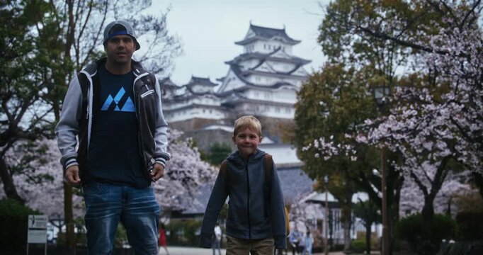 Father and son posing for camera in front of Himeji castle near cherry blossoms and playing games