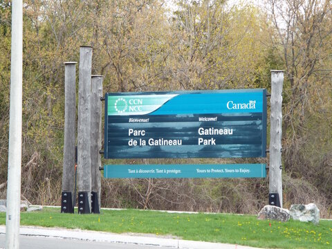 Gatineau, Quebec, Canada &ndash; May 8, 2026: A bilingual "Welcome" sign for "Gatineau Park, managed by the NCC", stands prominently against a wooded background on Gatineau, Quebec.