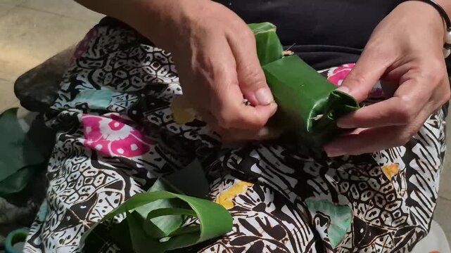 High angle view of senior woman making traditional Javanese snack wrapped in banana leaf