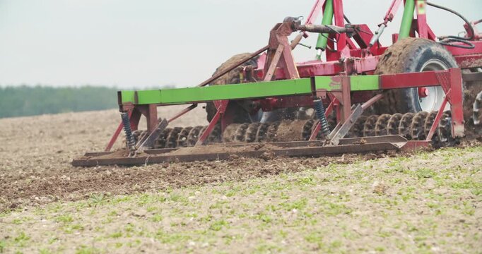 Rotary tiller churning wet soil in a rural farm field