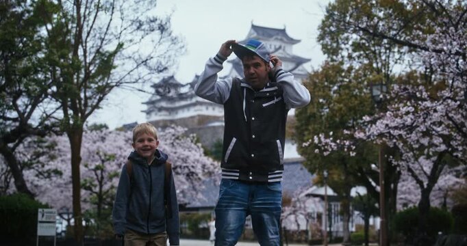 Father and son posing in front of cherry blossoms and ancient 17th century Japanese castle