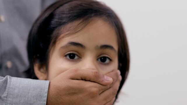 Scared young girl with an adult man's hand covering her mouth - child abuse. Close-up shot of a child being grabbed from behind to stop her from screaming - domestic violence 