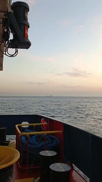 Vertical panoramic shot of a calm sea at sunset from a moving vessel deck, revealing a crescent moon in the sky.