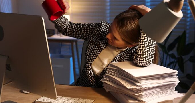 Workaholic. Tired woman checking empty coffee cup at wooden desk with computer and stack of documents indoors at night. Camera moving forward