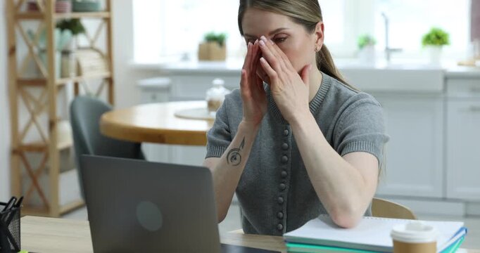 Workaholic. Overwhelmed woman at wooden desk with takeaway cup of coffee, laptop and stationery in kitchen. Camera moving forward