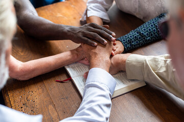 Naklejka premium Diverse group holding hands over a book on a wooden table.