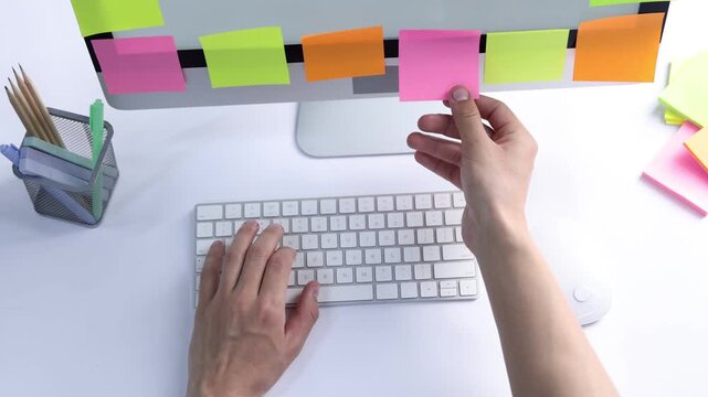 Man typing on computer keyboard and blank sticky notes at white table, top view. Multitasking, deadline and rush at work