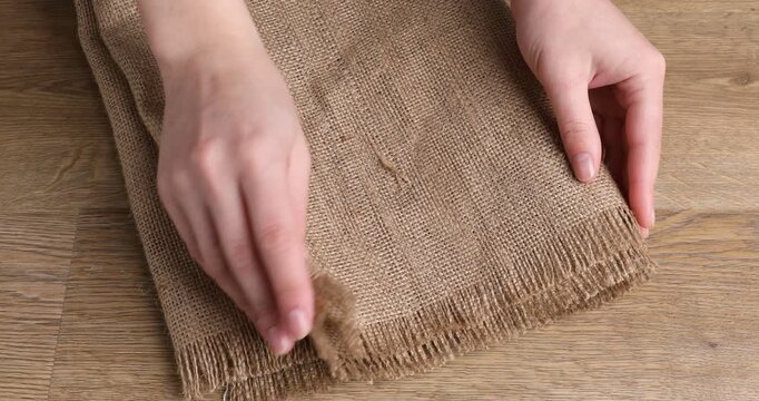 Woman with folded burlap fabric at wooden table, closeup
