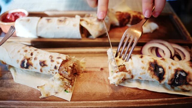 Close up of a freshly prepared wrap being sliced into portions on a wooden serving board, with sauces and side ingredients placed nearby