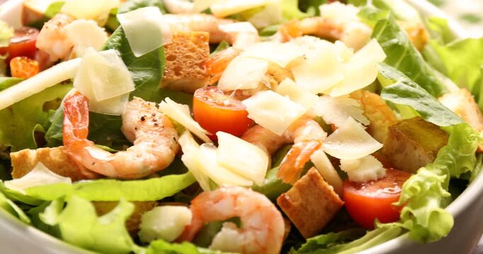 Delicious Caesar salad with shrimps in bowl on wooden table, closeup. Camera moving right