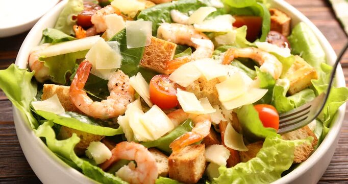 Woman eating delicious Caesar salad with shrimps at wooden table, closeup