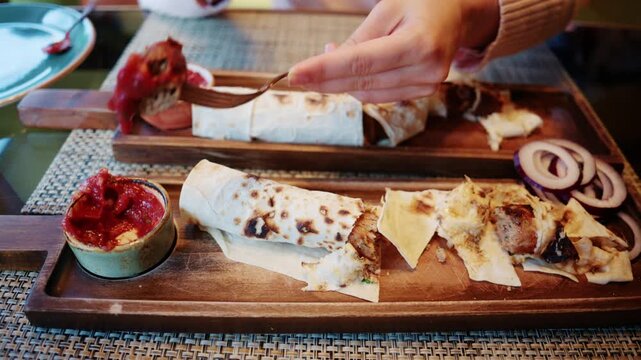 Close up of a freshly prepared wrap being sliced into portions on a wooden serving board, with sauces and side ingredients placed nearby