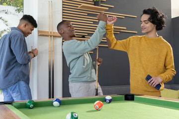 Obraz premium Diverse male teens celebrating by fist bumping near pool table with cues and smartphone