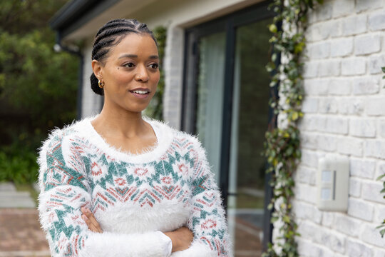 African American woman 30s standing by sliding glass door at house in fuzzy sweater arms crossed