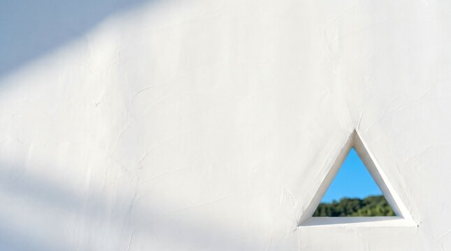 Minimalist white stucco castle wall with a geometric triangular loophole framing a slice of summer sky