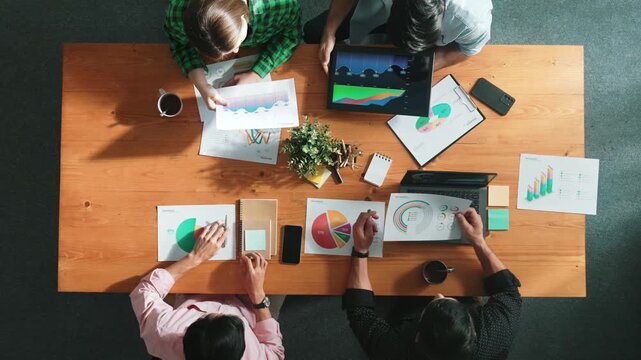 Top down aerial view of business man pointing and presenting at financial chart while diverse team discussing about stock market statistic at meeting table with laptop and graph document. Convocation.