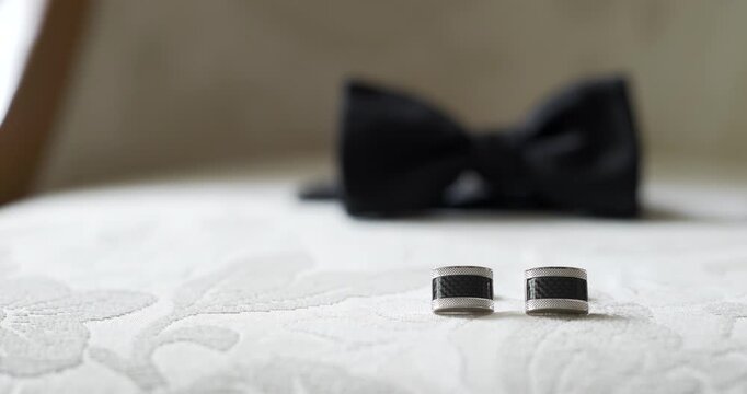 Wedding rings on white bedding with blurred bow tie