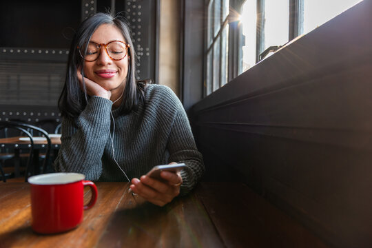 Person smiling, using a smartphone in a cozy cafe with a red mug.