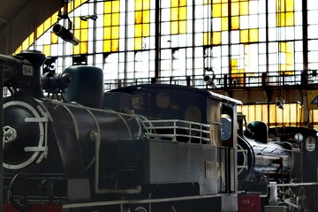 Vintage steam locomotives parked inside a grand old train station with large windows © Thanakrit