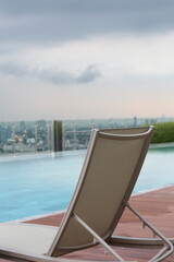 Fototapeta premium Relaxing lounger by infinity pool overlooking city skyline on a cloudy day