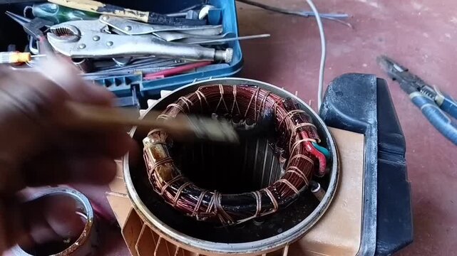 Close-up shot of a paint brush applying thick insulation varnish to the copper windings of an electric motor during a sustainable repair.