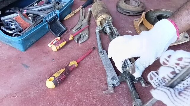 A technician wearing white gloves uses a bearing puller tool to extract a worn-out mechanical bearing from an electric motor's rotor shaft.