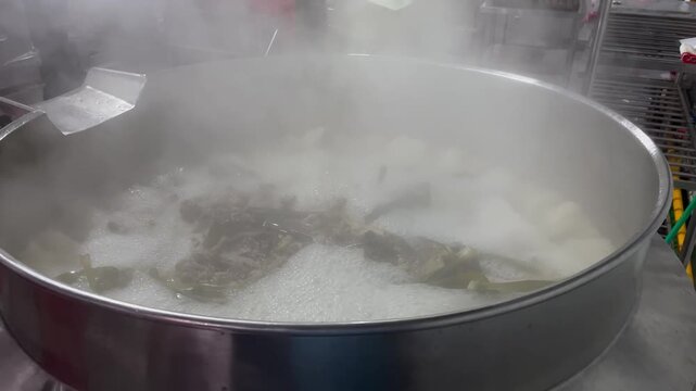 Steam rising from a boiling industrial kettle during beef stew production. Commercial food manufacturing process demonstrating steam cooking, temperature control, and large-scale batch preparation.